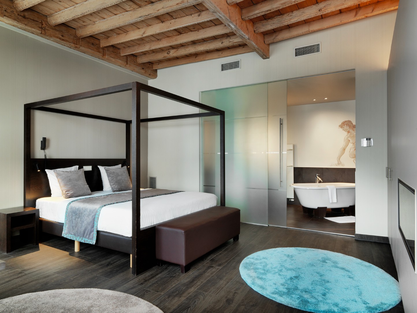 Hemelbed onder oude balken met ligbad in de kamer